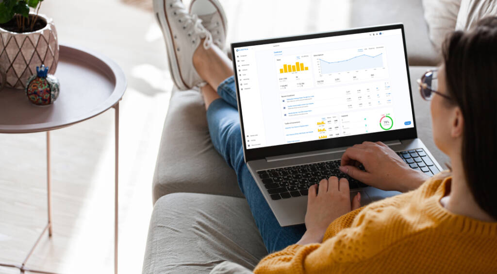 Woman using a laptop at home, looking at screen with dashboard user interface.